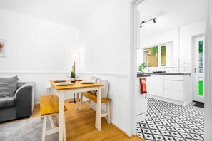 A modern apartment with a dining area, a grey sofa, and a kitchen with white cabinets and a black and white patterned floor. - 4 Bedroom House - Parking - Garden - Top Rated
 (Birmingham)