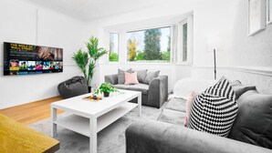 Una sala de estar moderna con un sofá blanco, sillones grises, una mesa de centro blanca y un ventanal con vistas a árboles.