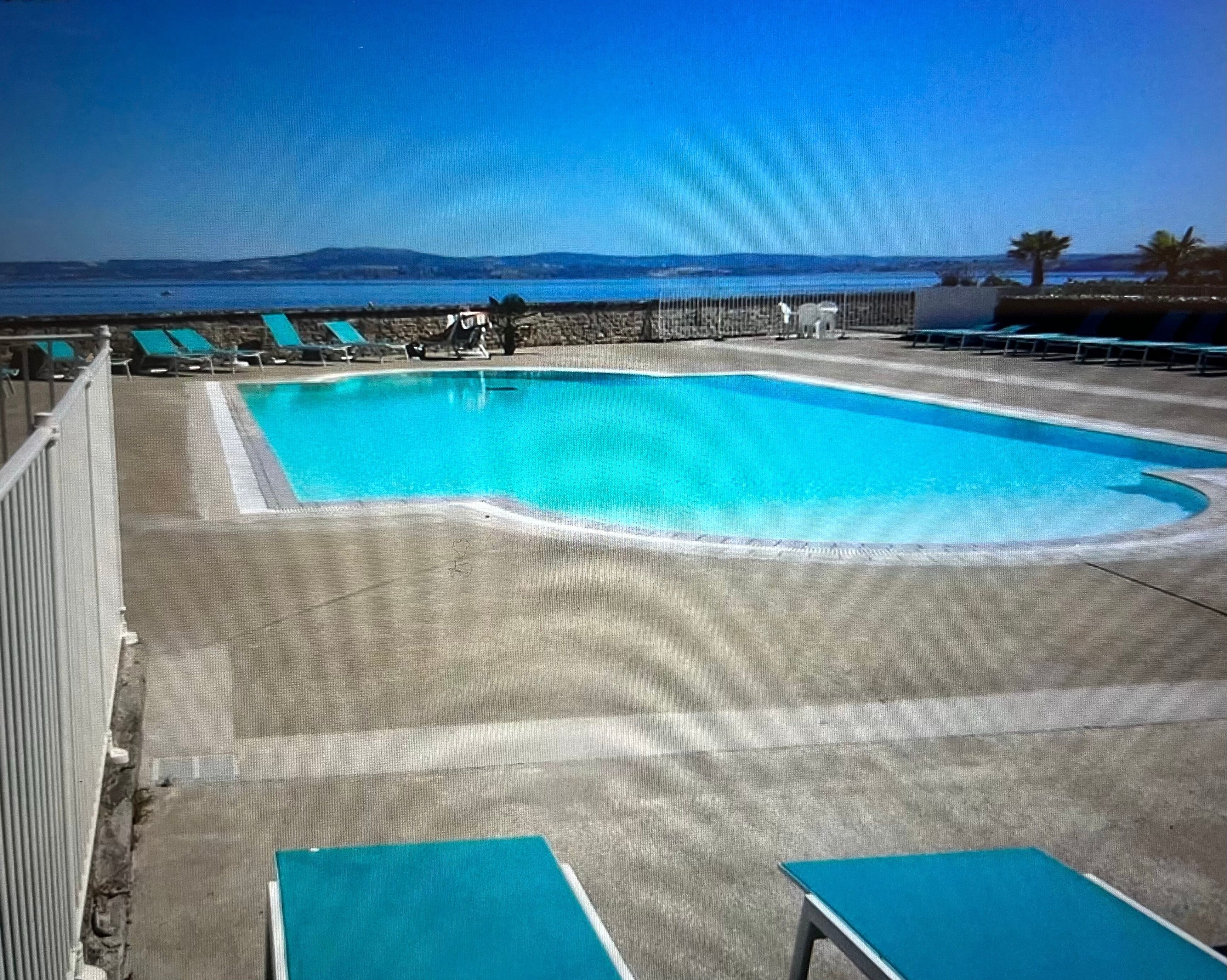 Uma piscina com espreguiçadeiras e vista para o mar.