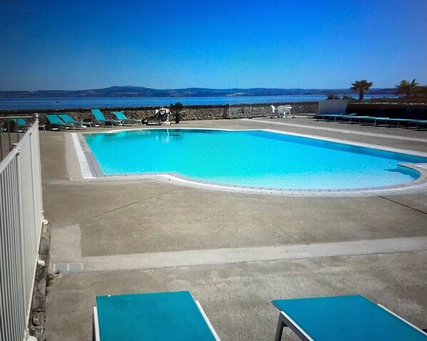 Une piscine avec des chaises longues et vue sur la mer.