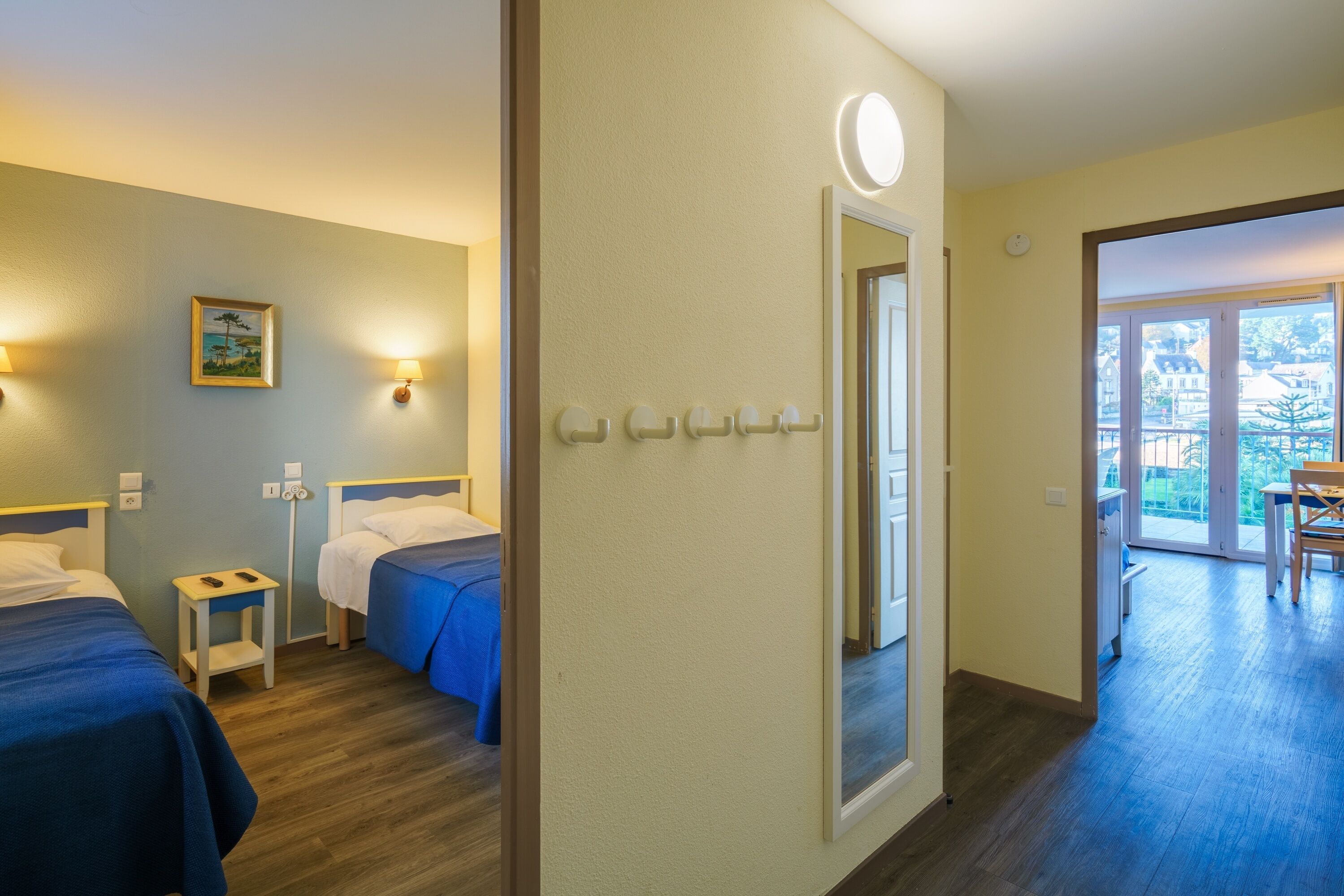 Et hotelværelse med to senge, et lille natbord, et spejl og en dør til en balkon.