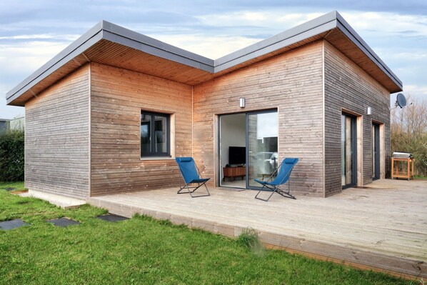 A modern house with a wooden exterior, a deck with two blue chairs, and a satellite dish.