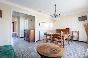 A dining area with a round wooden table, chairs, a kitchen with a microwave, and a television mounted on the wall.