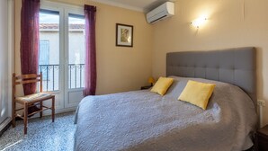 Une chambre à coucher avec un lit, deux oreillers, une chaise, une table de chevet, un climatiseur et une fenêtre avec des rideaux.