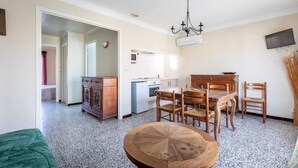 Un salon avec une table ronde en bois, un coin repas avec des chaises en bois, une cuisine avec un réfrigérateur blanc et un téléviseur fixé au mur.