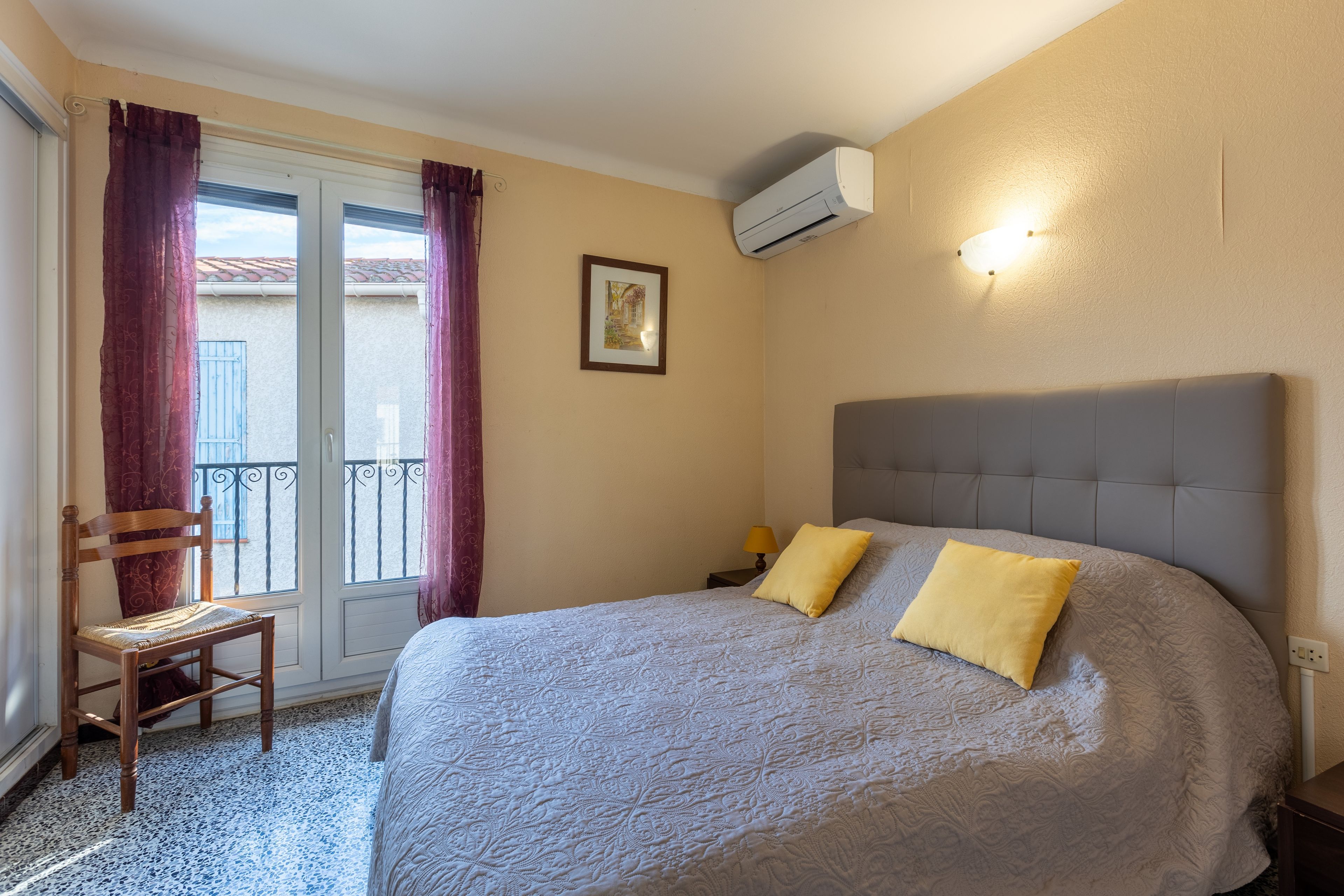 Une chambre à coucher avec un lit, une chaise, une fenêtre avec des rideaux et un appareil de climatisation.