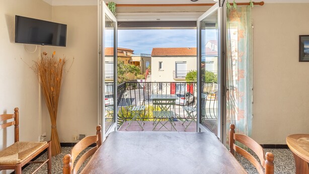 Un balcon avec une table et des chaises, un téléviseur fixé au mur et une vue sur la rue et les immeubles.
