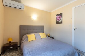 Et hotelværelse med seng, sengeborde, lampe, aircondition samt dør og vægmonteret lys.