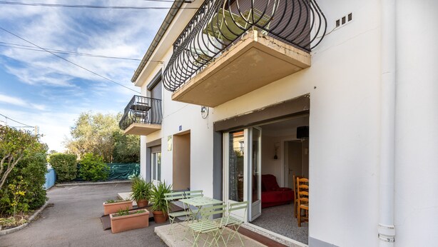A two-story building with a balcony, outdoor seating area with chairs and tables, and a red sofa inside.