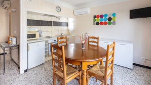 A compact kitchen with a microwave, toaster, and sink. There is a dining table with chairs and a clock on the wall.