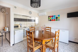 A compact kitchen with a dining area, a clock, and a color chart on the wall. - Pamplemousse - Appt à 10min d'Argelès-Sur-Mer (Saint-André)