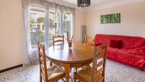 A dining area with a round wooden table and four chairs, a red sofa, a black hanging light fixture, and a green abstract painting on the wall.