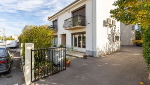 A two-story building with a balcony, potted plants, and a gated entrance.