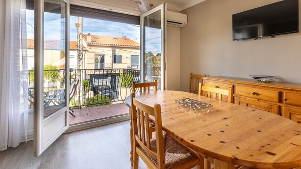 Ein Essbereich mit Holztisch und Stühlen, einem an der Wand montierten Fernseher und einer Glastür zum Balkon.