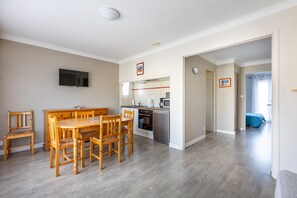 A modern kitchen with a dining area, a flat-screen TV mounted on the wall, and a hallway leading to a bedroom. - Mandarine - Appt à 10min d'Argelès-Sur-Mer (Saint-André)