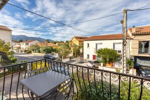 A balcony with a table and chairs, overlooking a street with parked cars and buildings.