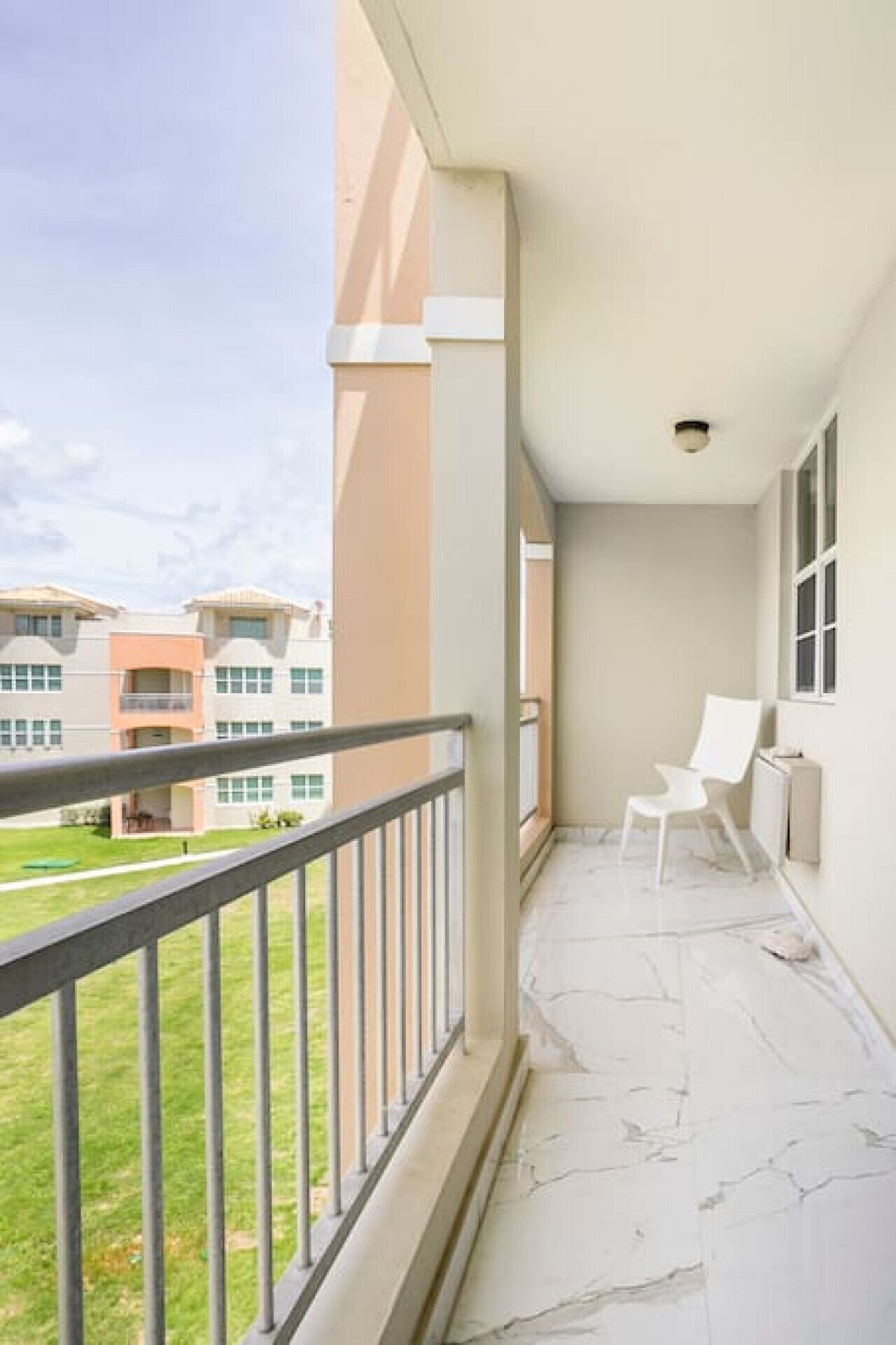 Un balcone con una sedia bianca, vista su un complesso di edifici e un'area verde.
