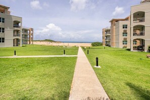A pathway leading to a beach with a view of the ocean, surrounded by multi-story buildings with balconies.