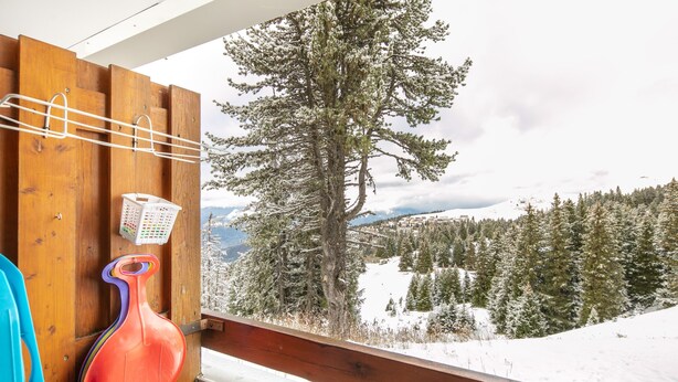Ein Balkon mit Holzgeländer, einer hängenden Wäscheständer mit Korb und Blick auf eine verschneite Berglandschaft.
