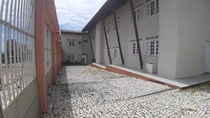 Une cour avec un sol pavé de pierres, des murs blancs et une clôture en métal.