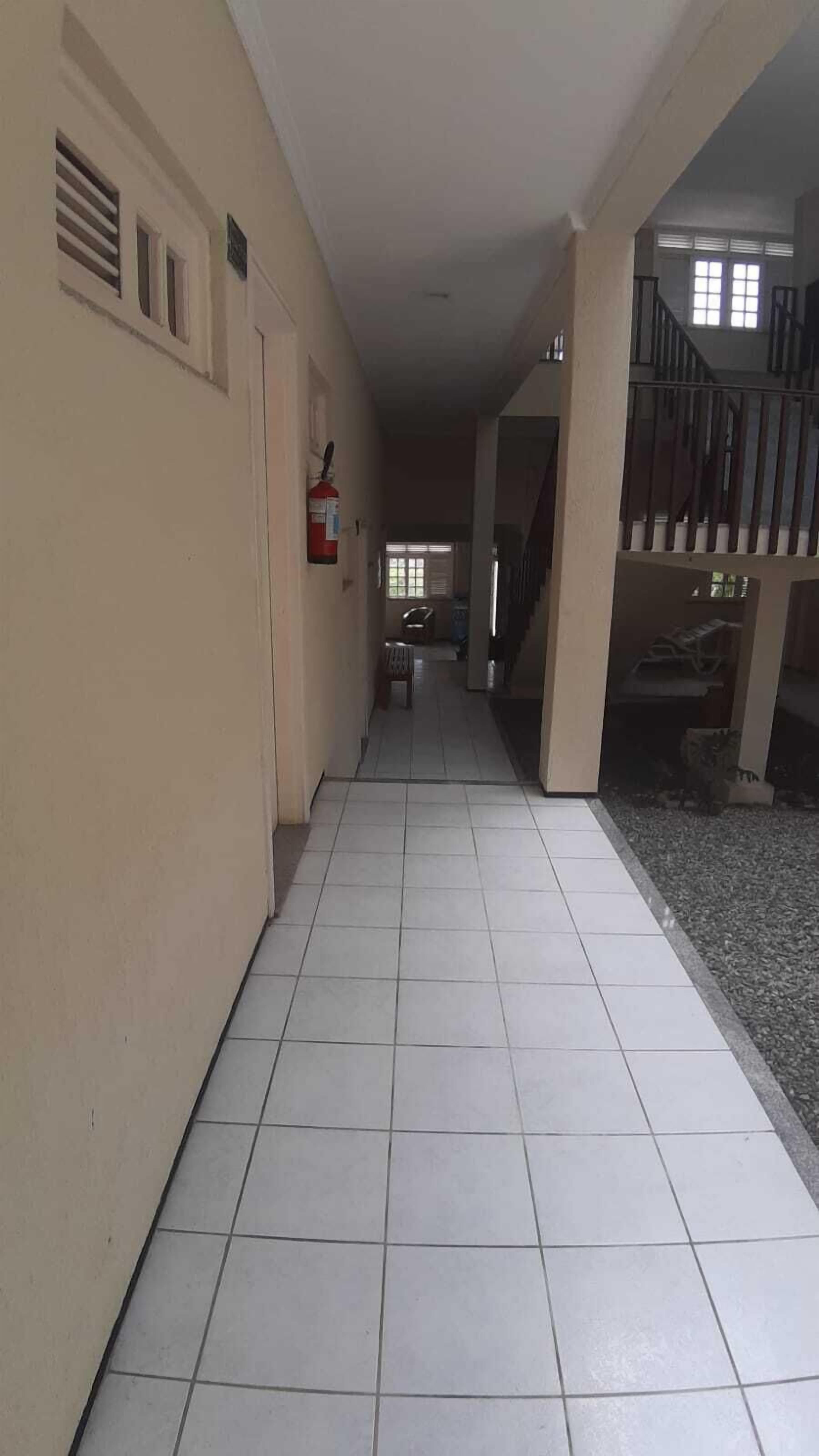A corridor with tiled flooring, a fire extinguisher mounted on the wall, and a staircase leading to an upper level.