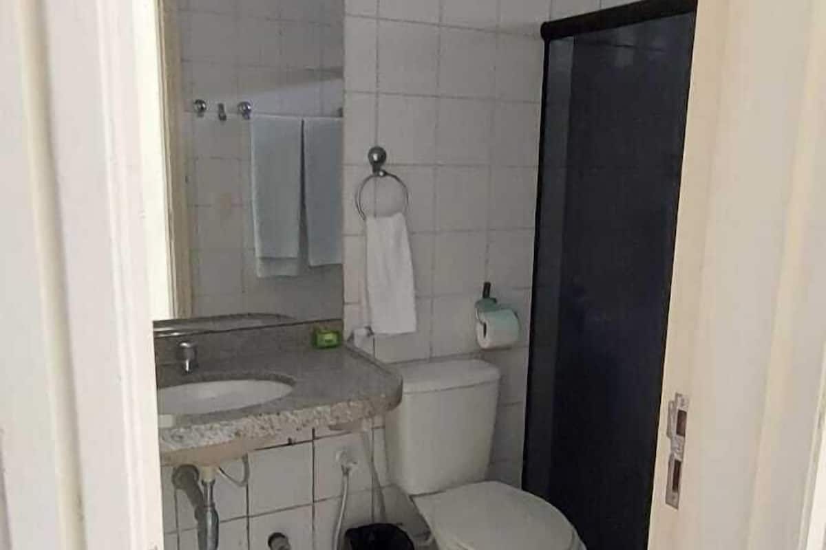 A small bathroom with white tiles, a toilet, a sink, and a mirror.