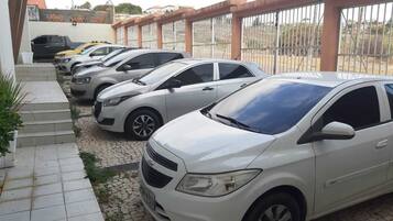 Fila de coches aparcados en un área de estacionamiento techada, con un paseo de baldosas que conduce a la entrada de un edificio.