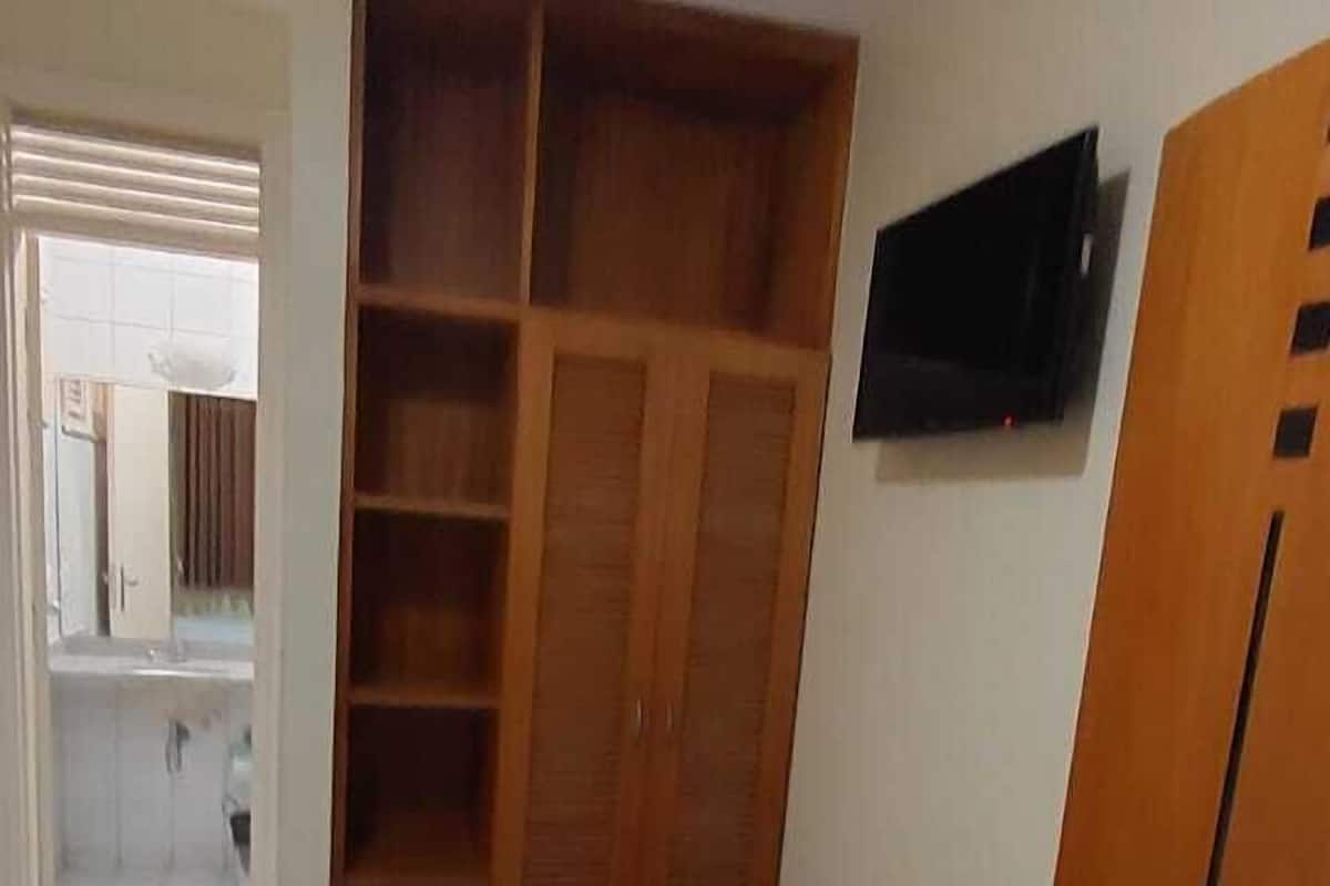 A bedroom with a bed, a wooden wardrobe, a desk, and a chair.