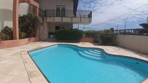 Une piscine dotée d’une terrasse carrelée, entourée d’un petit muret et bordée d’un bâtiment avec un balcon.