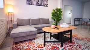 A modern living room with a grey sectional sofa, a wooden coffee table, a potted plant, and a painting on the wall. - résidence helios (Villeneuve-Saint-Georges)