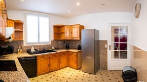 A compact kitchen with wooden cabinets, a stainless steel refrigerator, a dishwasher, and a window providing natural light. - résidence helios (Villeneuve-Saint-Georges)