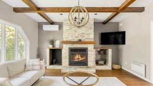 A living room with a stone fireplace, a sofa, a television, and a chandelier. - Hôtel à la maison - Beaufranc chalet (Inverness)