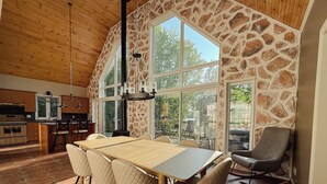 A spacious kitchen with a stone accent wall, large windows, and a dining area with a table and chairs. - Hôtel à la maison - Beaufranc chalet (Inverness)