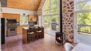 A spacious kitchen with wooden cabinets, a large island with bar stools, a stone wall, and a fireplace. - Hôtel à la maison - Beaufranc chalet (Inverness)