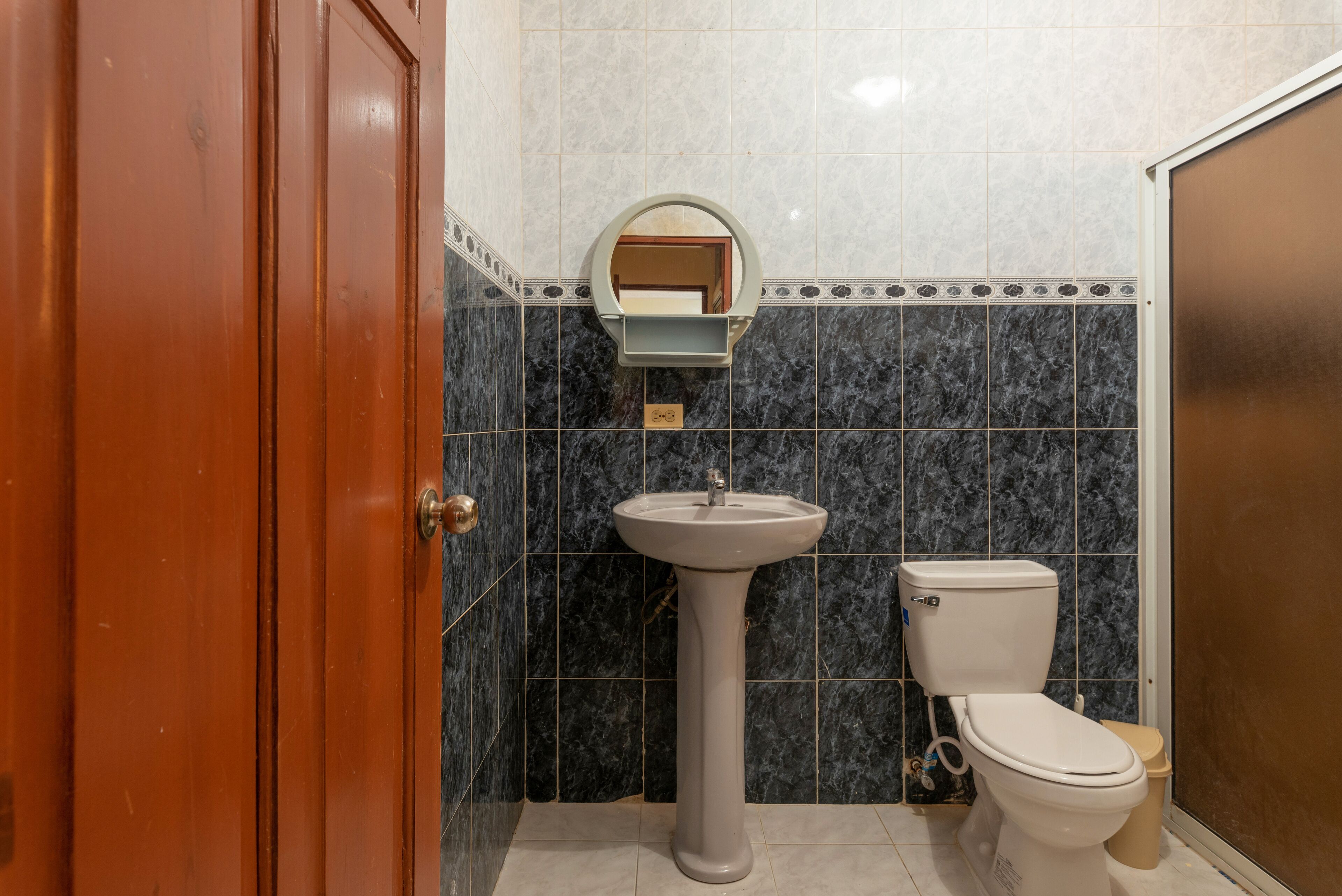 Un baño con lavamanos pedestal, inodoro y puerta de madera.