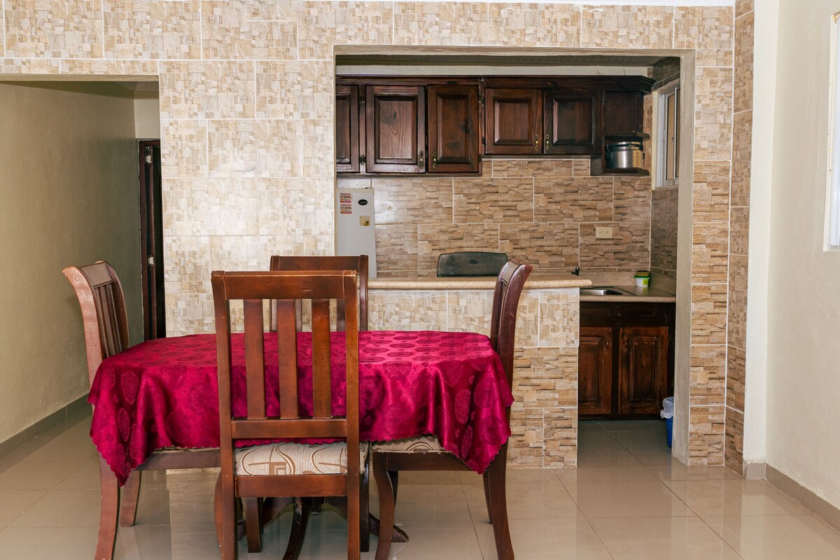 A dining area with a table set for two, wooden chairs, and a red tablecloth.