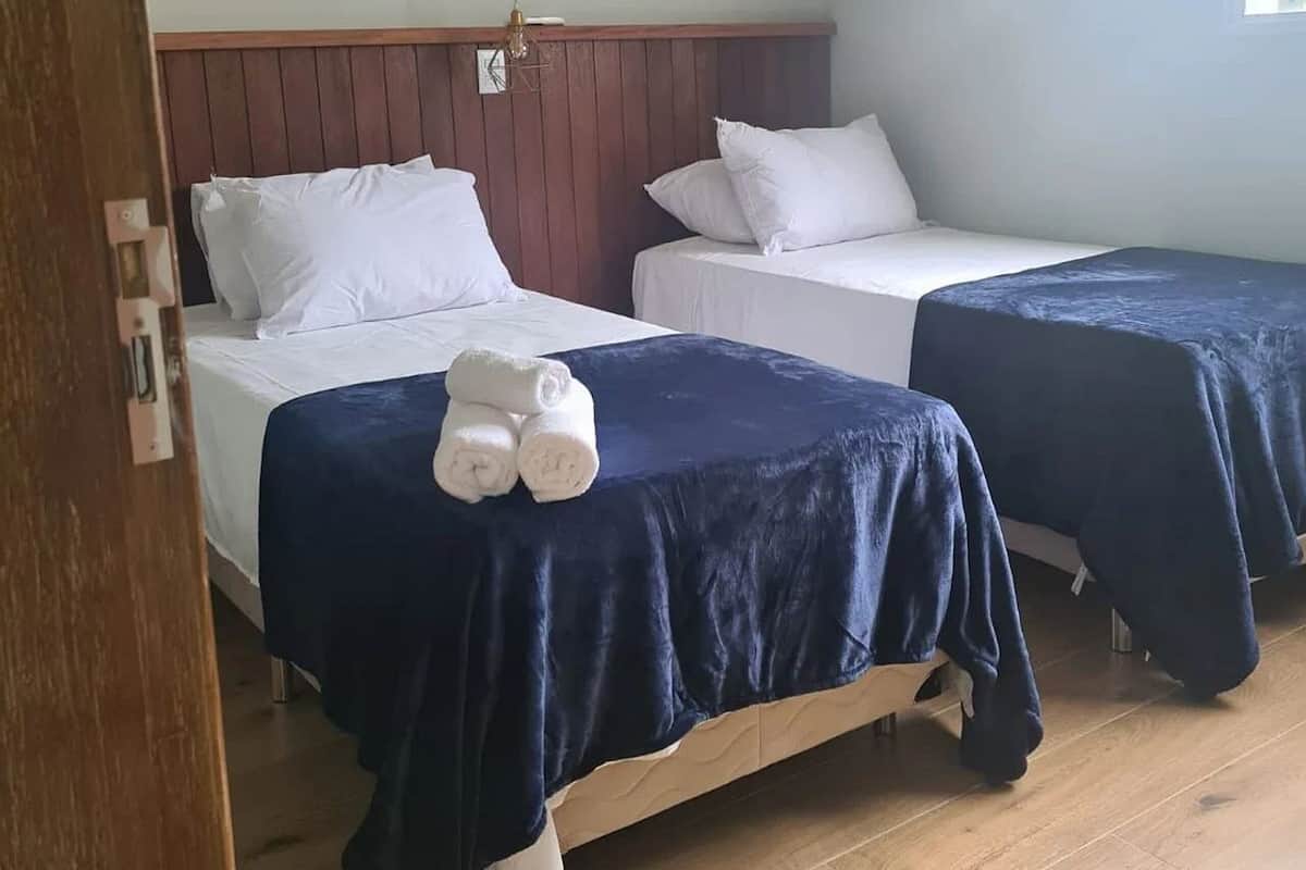 A room with two beds, each with white bedding and a dark blue cover. There are white towels on the beds. The room has wooden flooring and a light-colored wall.