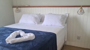 A neatly made bed with white linens and a blue bedspread, a white towel folded on the bed, and a wooden headboard. - Casa de Alto Padrão Condomínio Privado (Chapada dos Guimarães)