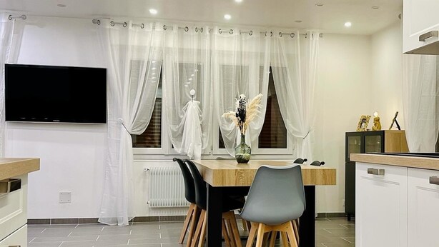 A modern kitchen with a dining area, white cabinetry, a flat-screen TV, and a window with sheer curtains. - Res. Marie Galante Lac du Der (Moncetz-l'Abbaye)