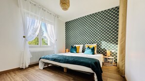 A bedroom with a bed, a window with sheer curtains, a wall with a geometric pattern, and a wooden floor. - Res. Marie Galante Lac du Der (Moncetz-l'Abbaye)