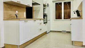 A modern kitchen with white cabinetry, a wooden countertop, an oven, and a window with blinds. - Res. Marie Galante Lac du Der (Moncetz-l'Abbaye)