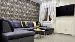 A modern living room with a grey sectional sofa, a small round coffee table, and a flat-screen TV mounted on the wall. - Res. Marie Galante Lac du Der (Moncetz-l'Abbaye)