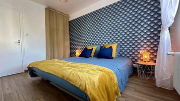 A bedroom with a bed, a headboard with a wave pattern, a bedside table with a lamp, and a curtain.