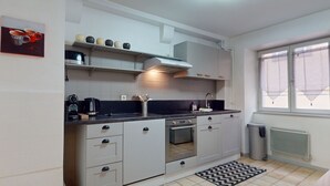 A modern kitchen with white cabinets, a black countertop, a built-in oven, and a window with sheer curtains. - Gite de Paul - centre ville Colmar (Colmar)