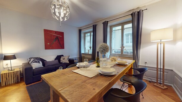 A modern living room with a wooden dining table, black chairs, a sofa, and a chandelier. - Gite de Paul - centre ville Colmar (Colmar)