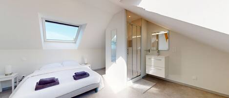 A bedroom with a skylight, a bed, a bedside table, a mirror, and a bathroom with a sink and mirror.