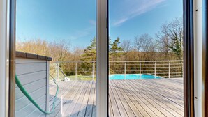 Una terraza de madera con piscina, rodeada por una valla metálica y árboles.