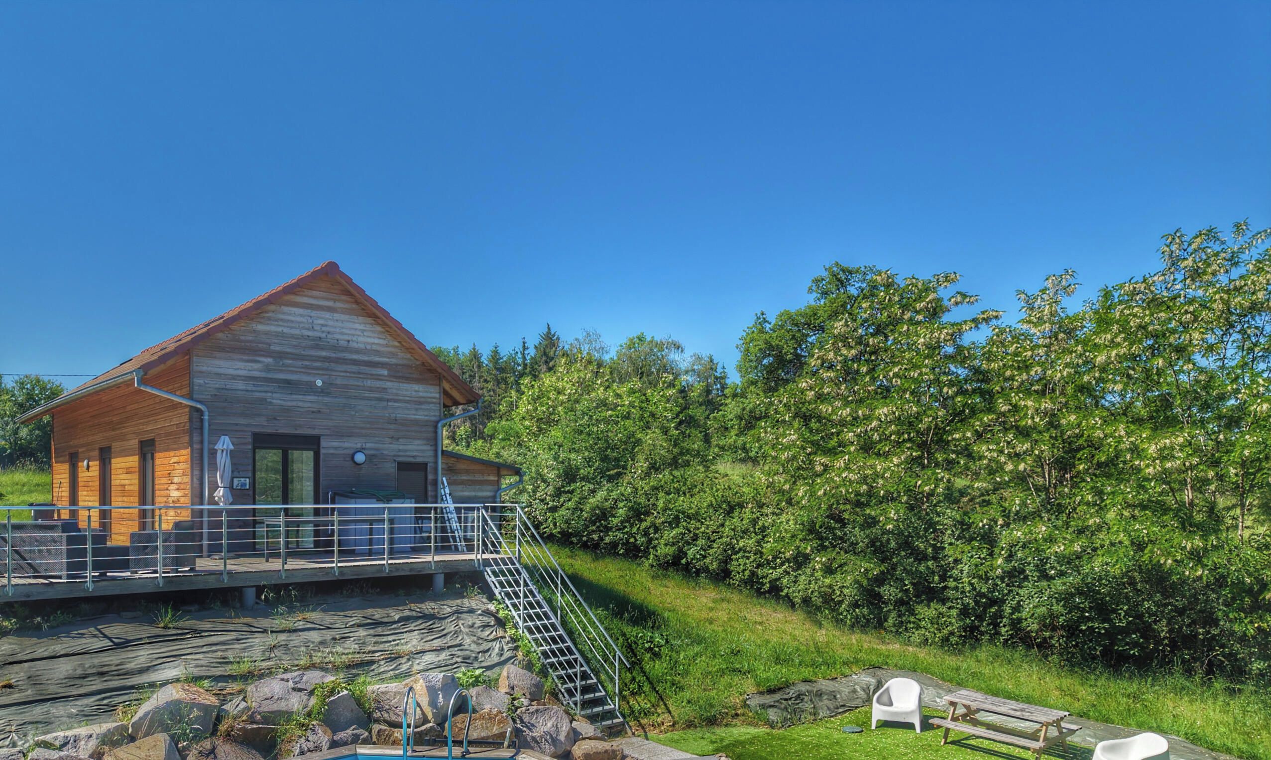 A wooden cabin with a balcony, a staircase leading to a deck, and a pool area.