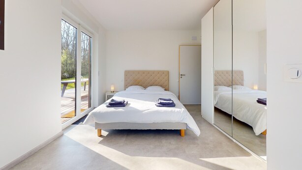 Un dormitorio moderno con una cama grande, una puerta corredera que da a un área exterior y un armario con espejo.
