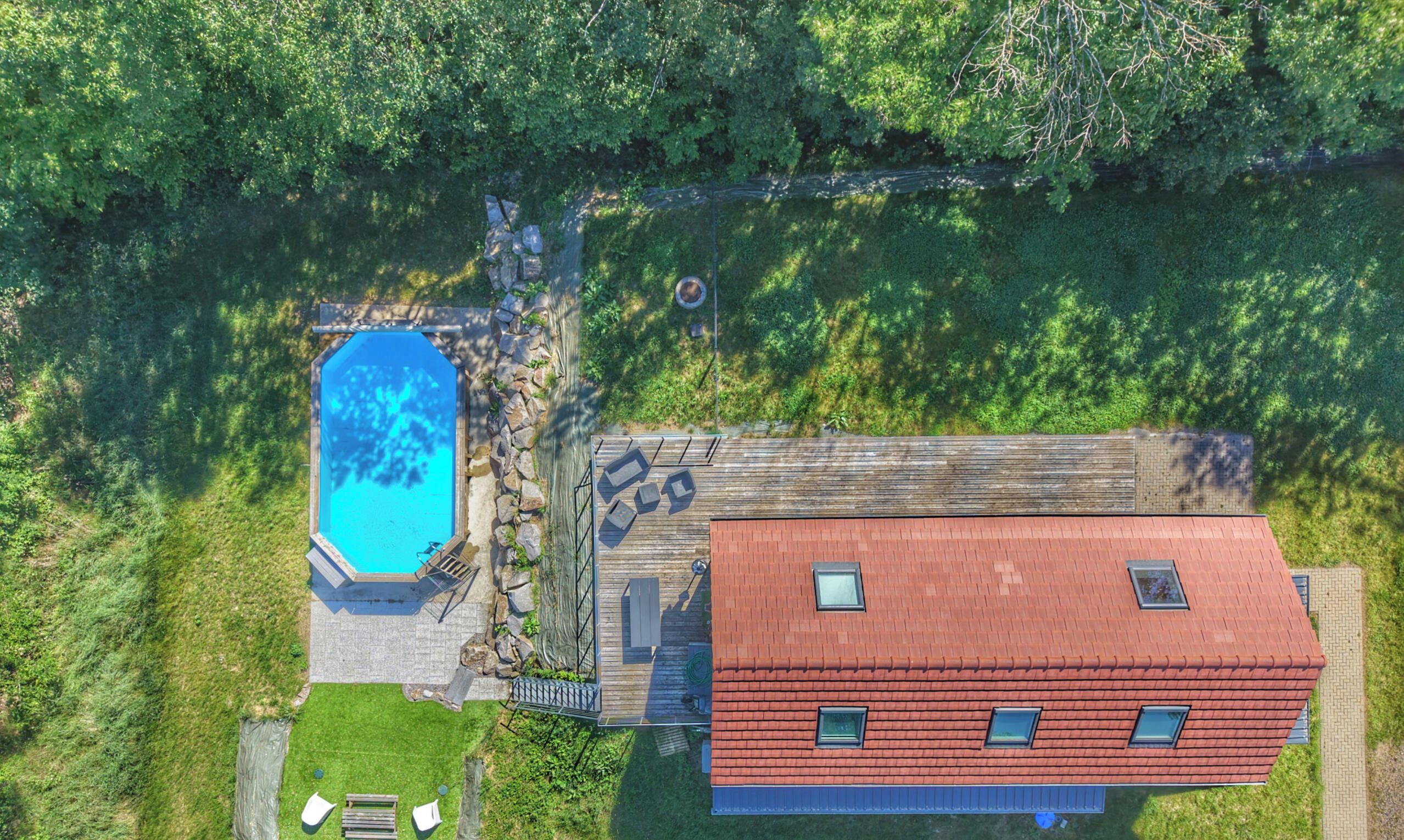 Vista aérea de una propiedad con piscina, terraza de madera y un edificio de techo rojo.